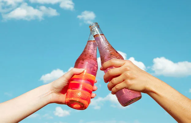 two people clinking soda bottles
